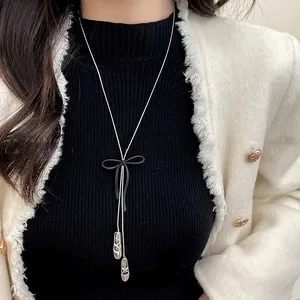 Silver Y-necklace featuring black bow and ballet slipper pendants on a model wearing tweed
