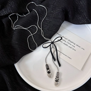 Detailed macro view of silver ballet shoe pendants with black bow on a long snake chain