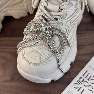 Close-up of beige platform sneakers featuring silver beaded chain charms on laces