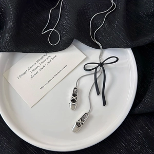 Detailed macro shot of silver ballet shoe pendants and black 3D bow on snake chain necklace