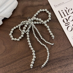 Close-up of handmade silver beaded bow charm on a minimalist dark wood surface