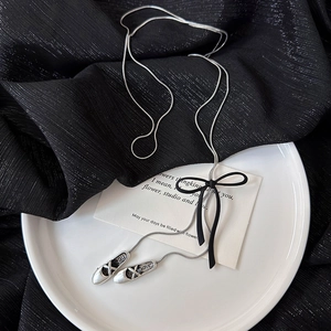 Detail of silver ballet shoe pendants and black silk bow on a long snake chain necklace