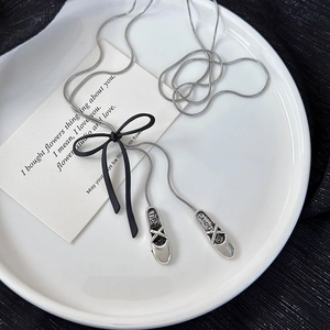 Detail of ballet shoes pendants with heart engraving and black matte bow on a silver chain