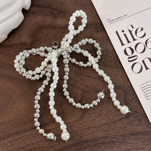 Detail of beaded bow shoe charm with white pearls and silver metal tassels on wood