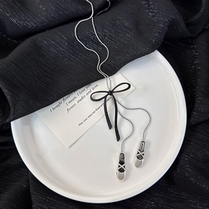 Detail of silver ballet shoe pendants and black ribbon bow on a long snake chain necklace