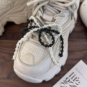 Close-up of a stylish beige sneaker decorated with a handmade pearl bow shoe lace charm