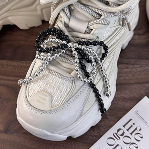 Detail of pearl bow and beaded tassel accessory on off-white platform sneaker