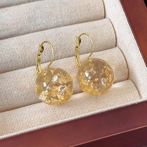 Vista dettagliata di orecchini a sfera in resina con foglia d'oro in una scatola regalo