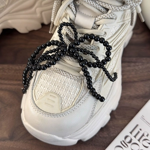 Detail of beaded black bow charm on cream chunky sneaker with mixed material texture