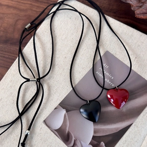 Adjustable cord necklace with red and black heart pendants on a textured background