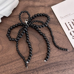 Detail of handmade black beaded bow charm with metal lobster clasp on a vintage wood surface