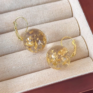 Dettaglio macro di orecchini in resina ambrata con foglie d'oro e ganci a sfera
