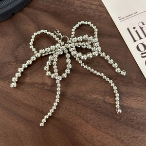 Silver beaded bow charm with lobster clasp for shoes and bags on wooden table