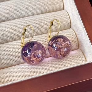 Dettaglio di orecchini in resina viola con foglia d'oro su fodera di portagioie morbido