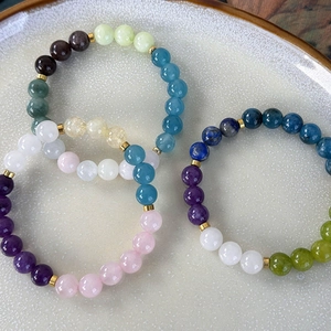 Colorful gemstone beaded bracelets with golden spacers for women in a ceramic dish