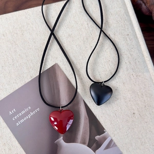 Minimalist red heart pendant necklace with adjustable black cord on textured background