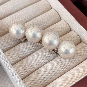 Détail de quatre grandes perles crème sur une barrette à cheveux en métal brillant