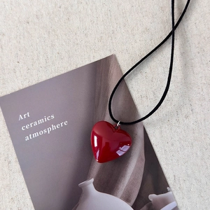 Close-up of bright red heart pendant with adjustable black cord on textured background