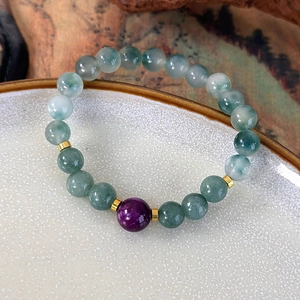 Close-up of handmade beaded bracelet with light green jade beads and purple stone accent