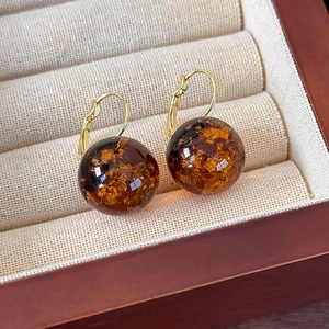 Dettaglio macro di orecchini a sfera in resina ambrata con foglia d'oro in scatola