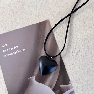 Macro shot of matte black heart pendant on adjustable black cord over beige fabric