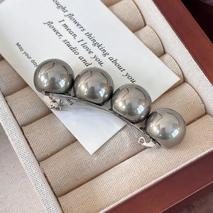 Détail de grandes perles grises sur une pince à cheveux en métal dans un écrin à bijoux