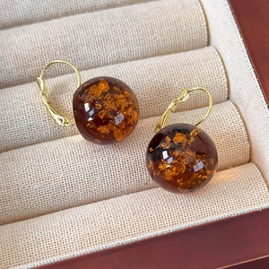 Dettaglio di orecchini a sfera in resina ambrata con foglie d'oro in scatola beige