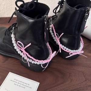 Détail d'une chaîne de chaussure en perles avec nœud rose sur des bottes noires avec clip