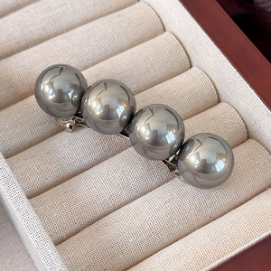 Détail macro de quatre perles gris foncé brillantes sur une barrette à ressort argentée