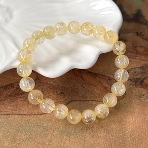 Macro detail of natural rutilated quartz beaded bracelet on a white decorative shell tray