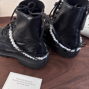Détail de chaînes en perles et nœuds en ruban noir sur bottines en cuir noir