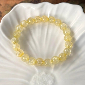 Detail view of natural yellow crystal beads with internal textures on a white shell tray