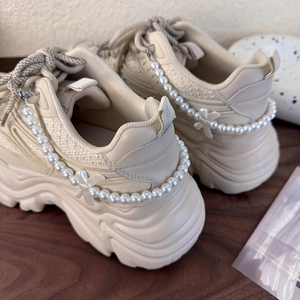Detail der abnehmbaren Perlenkette und Schleifen am Absatz eines cremefarbenen Sneakers