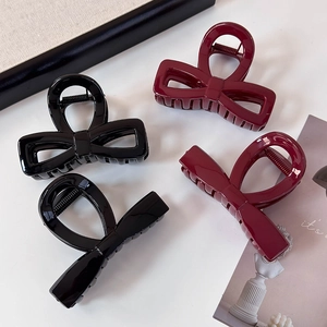 Detail view of black and wine red bow hair claws and cross shark clips on white surface