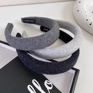 Close-up of three thick knitted headbands in grey tones featuring handmade inner labels