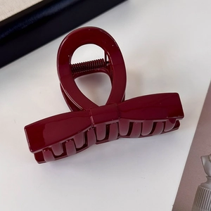 Macro shot of a glossy dark red bow hair claw clip with a secure metal spring mechanism