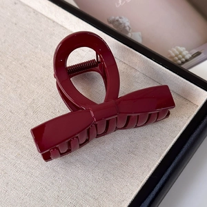 Detailed close-up of a burgundy bow hair claw clip with glossy acrylic finish