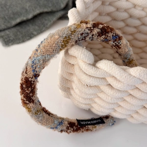 Detail shot of multi-colored tweed headband with a handmade label on a white basket