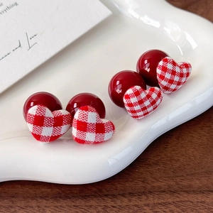 Close-up of red beads and red-white checkered fabric heart earrings on ceramic tray