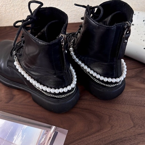 Detailansicht schwarzer Springerstiefel mit eleganten Perlen- und Metallkettenverzierung