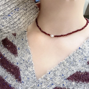 Elegant beaded necklace with deep red faceted stones and white pearl on knitted sweater