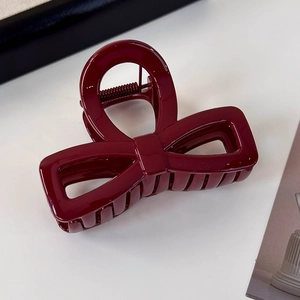 Close-up of a glossy burgundy red bow hair claw clip with a secure metal spring