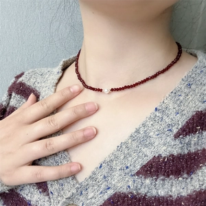 Detailed view of red garnet beads and central pearl necklace on female collarbone