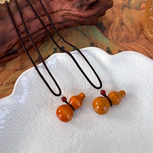 Détail de deux pendentifs calebasse en bois sur des cordons marron tissés avec des perles