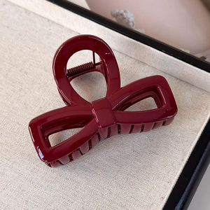 Detail of glossy deep red bow-shaped hair claw clip with a polished finish and metal spring
