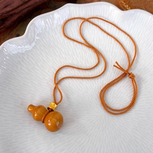 Détail du pendentif gourde en bois avec corde tressée et perle dorée sur plat céramique