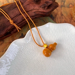 Détail d'un pendentif gourde poli couleur ambre avec perle dorée sur cordon tressé