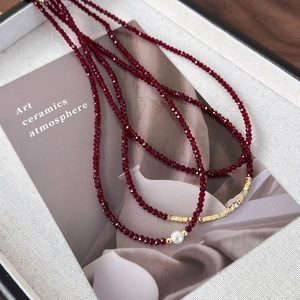Detailed close-up of red beaded necklace with golden accents and a single white pearl