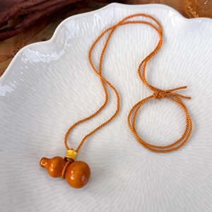 Détail du pendentif gourde ambré sur un collier à cordon tressé orange vif