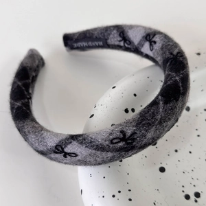 Macro shot of grey plaid knit headband featuring black bow patterns and handmade label tag